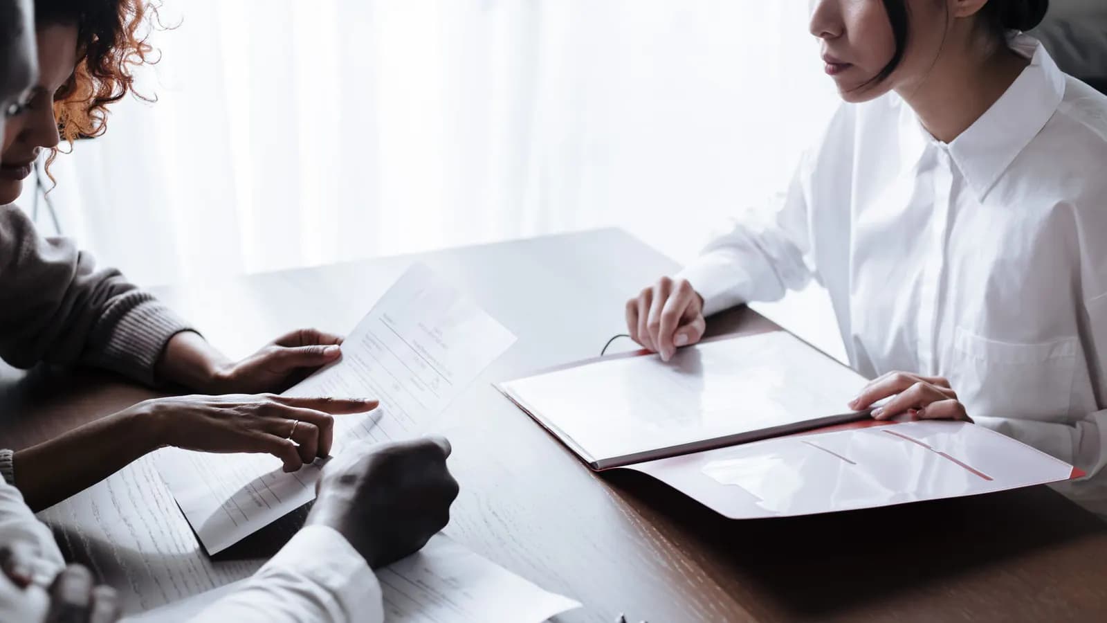 Two people review a printed form while a woman across the table holds an open folder of papers